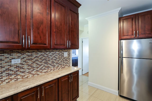 kitchen with light tile patterned floors, light stone counters, freestanding refrigerator, crown molding, and backsplash