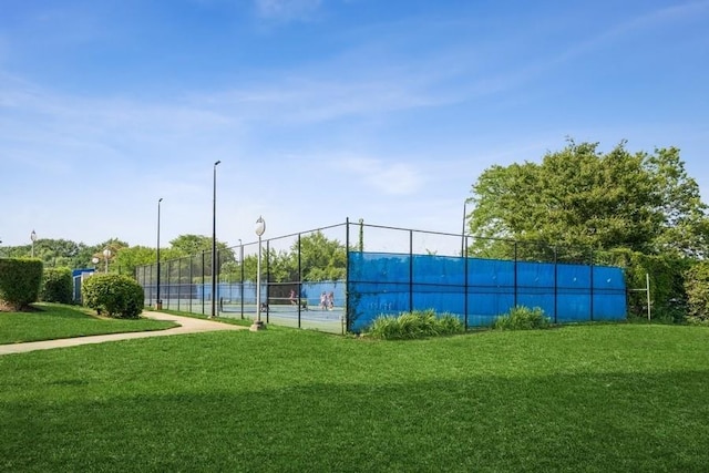 view of sport court with fence and a lawn