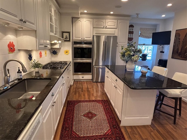 kitchen featuring under cabinet range hood, stainless steel appliances, dark wood-type flooring, a sink, and a kitchen bar