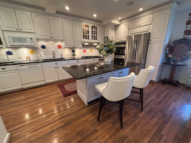 kitchen featuring dark wood-style floors, dark countertops, a sink, white appliances, and a kitchen breakfast bar