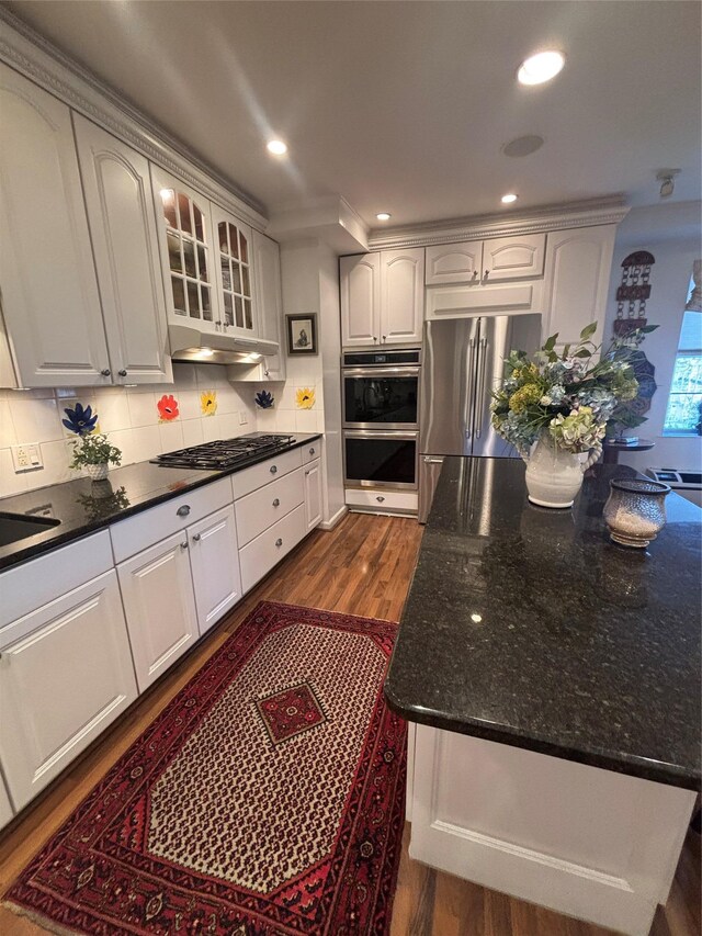 kitchen with appliances with stainless steel finishes, dark stone counters, glass insert cabinets, and decorative backsplash