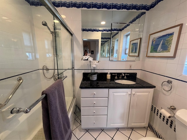 full bath with radiator heating unit, combined bath / shower with glass door, tile walls, and vanity