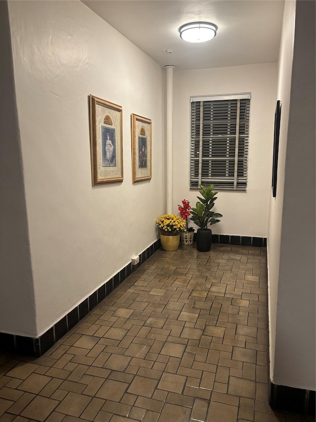 hall featuring brick floor and baseboards