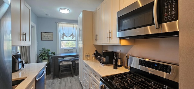 kitchen featuring stainless steel appliances, light wood-type flooring, white cabinetry, and light stone countertops