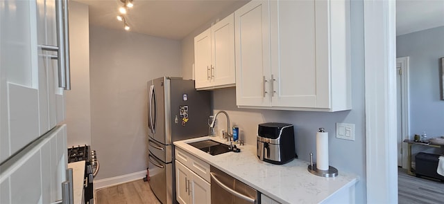 kitchen featuring light stone counters, light wood finished floors, stainless steel appliances, white cabinets, and a sink