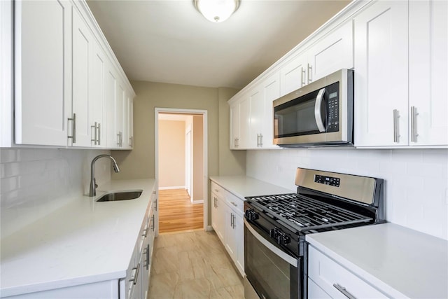 kitchen with stainless steel appliances, a sink, white cabinets, light countertops, and decorative backsplash