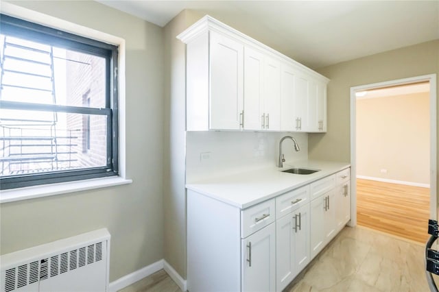 kitchen featuring a healthy amount of sunlight, a sink, radiator heating unit, and white cabinetry