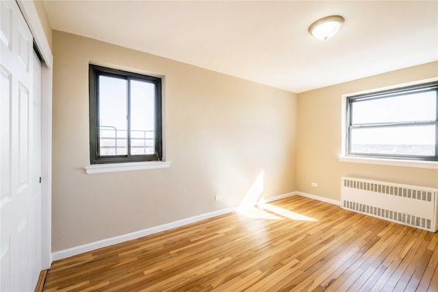 empty room with baseboards, hardwood / wood-style floors, and radiator heating unit