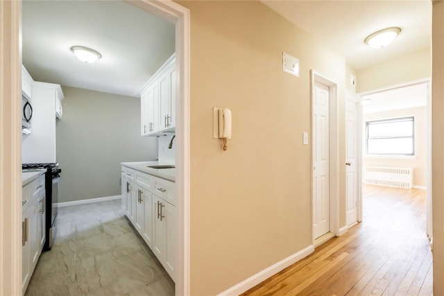 interior space featuring light wood-style floors, baseboards, a sink, and radiator heating unit