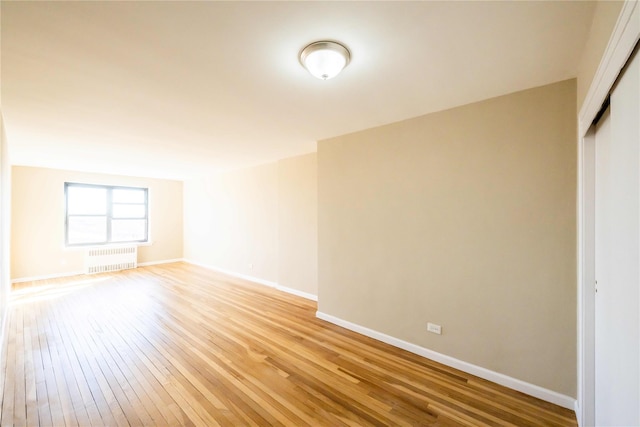 spare room with radiator, light wood-style floors, and baseboards