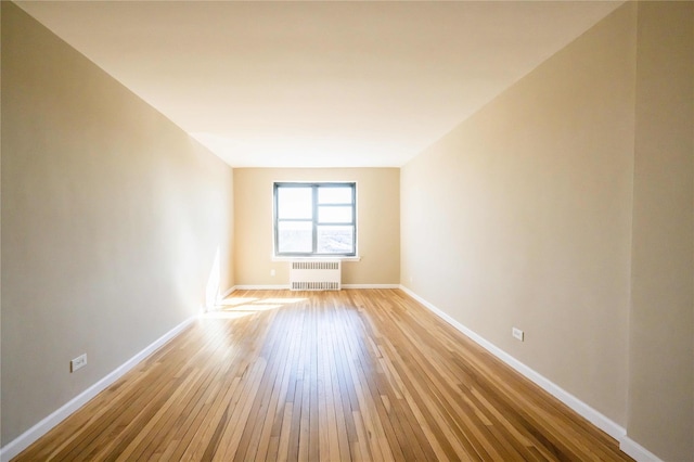 empty room with light wood-type flooring, radiator heating unit, and baseboards