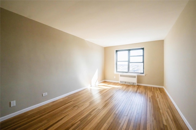 empty room with hardwood / wood-style floors, radiator heating unit, and baseboards