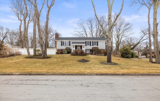 split foyer home featuring a chimney, fence, and a front lawn