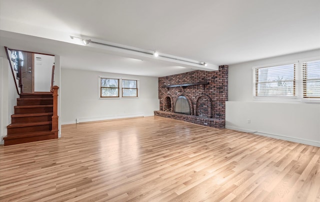 unfurnished living room featuring a brick fireplace, stairway, light wood-type flooring, and a baseboard radiator