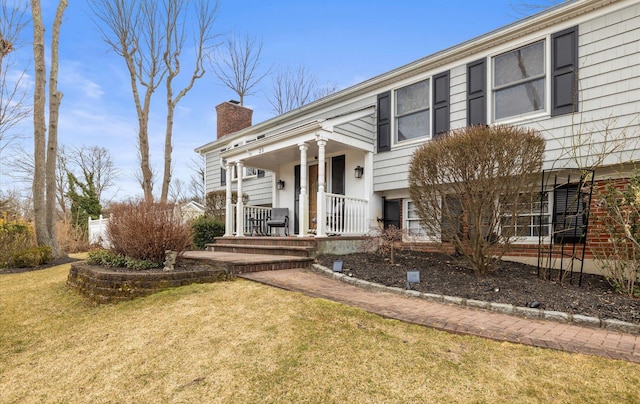 split foyer home with covered porch, a chimney, and a front lawn