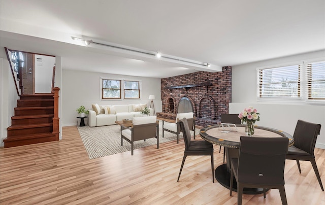 dining space with a fireplace, light wood-style floors, and stairs