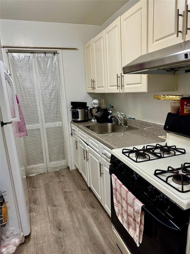 kitchen featuring white cabinets, range with gas cooktop, wood finished floors, freestanding refrigerator, and a sink