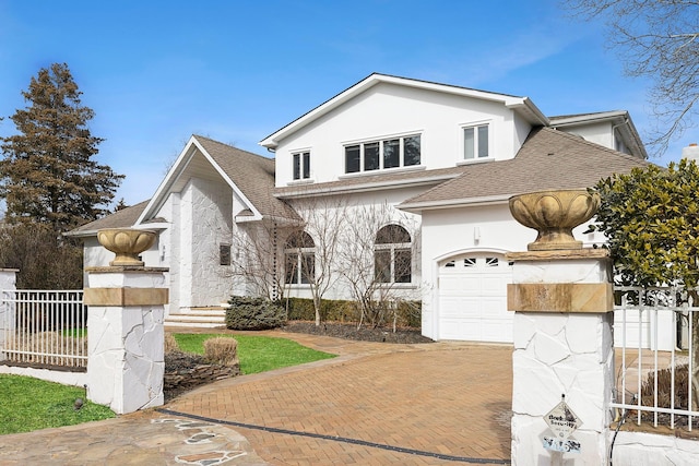 view of front facade with decorative driveway, roof with shingles, fence, and stucco siding