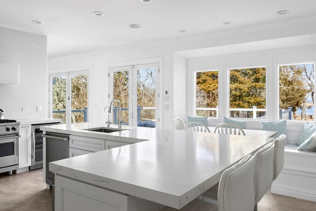 kitchen with a sink, ornamental molding, appliances with stainless steel finishes, light stone countertops, and a large island with sink