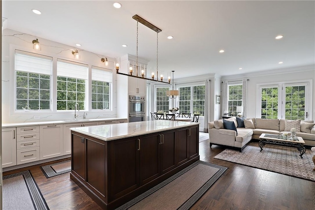 kitchen featuring stainless steel double oven, dark wood-type flooring, a kitchen island, a sink, and white cabinetry