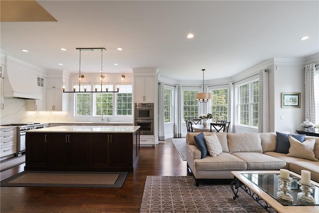 living area with a chandelier, a healthy amount of sunlight, dark wood-type flooring, and ornamental molding