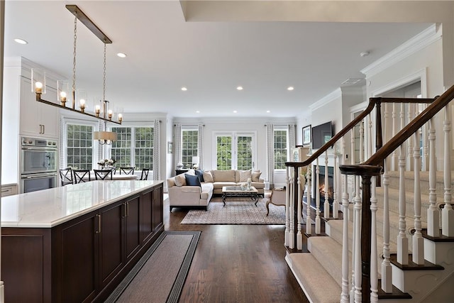 kitchen featuring dark brown cabinetry, dark wood-type flooring, crown molding, stainless steel double oven, and recessed lighting