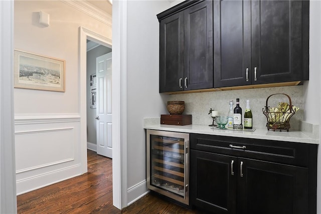 bar with dark wood-style floors, backsplash, ornamental molding, a bar, and beverage cooler