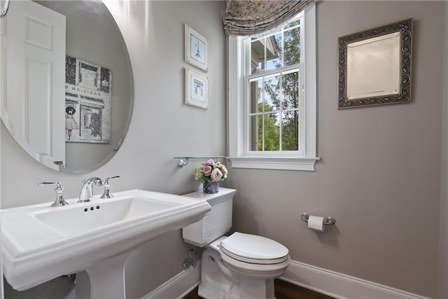 half bathroom with baseboards, a sink, and toilet