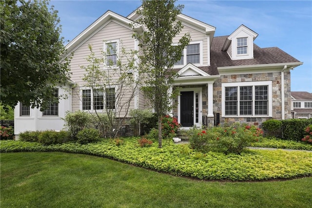 view of front of home with stone siding, a front lawn, and roof with shingles