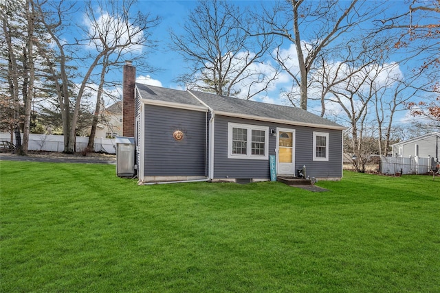 back of house featuring a chimney, fence, and a lawn