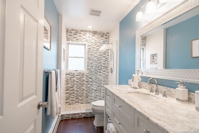 full bath featuring toilet, wood finished floors, vanity, visible vents, and tiled shower