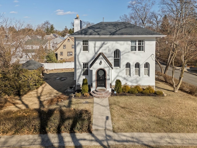 view of front of house featuring a shingled roof, a chimney, fence, a front lawn, and stucco siding