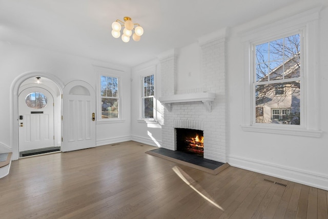 unfurnished living room with visible vents, a brick fireplace, wood finished floors, a chandelier, and baseboards