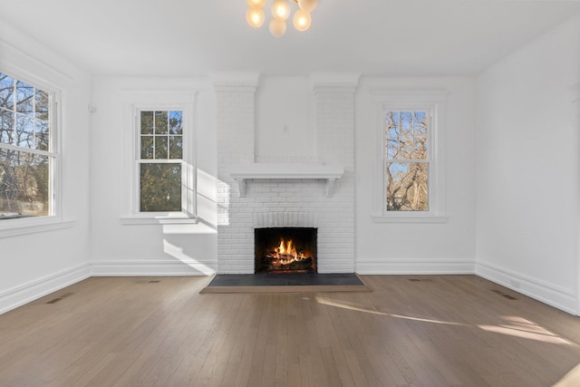 unfurnished living room featuring a wealth of natural light, wood-type flooring, a fireplace, and baseboards