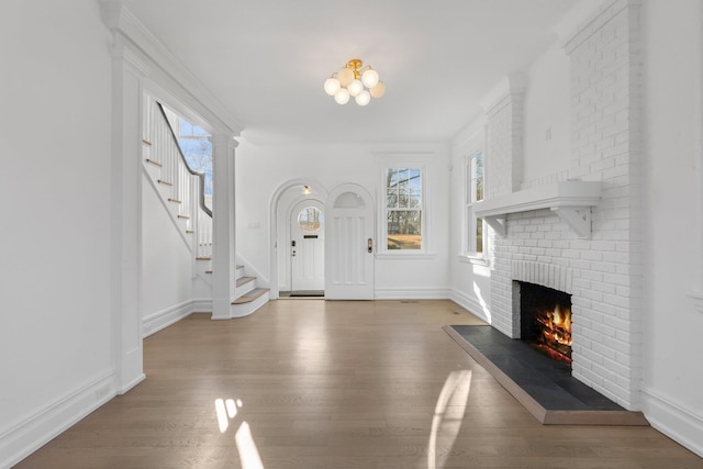 entryway featuring a brick fireplace, stairs, baseboards, and wood finished floors