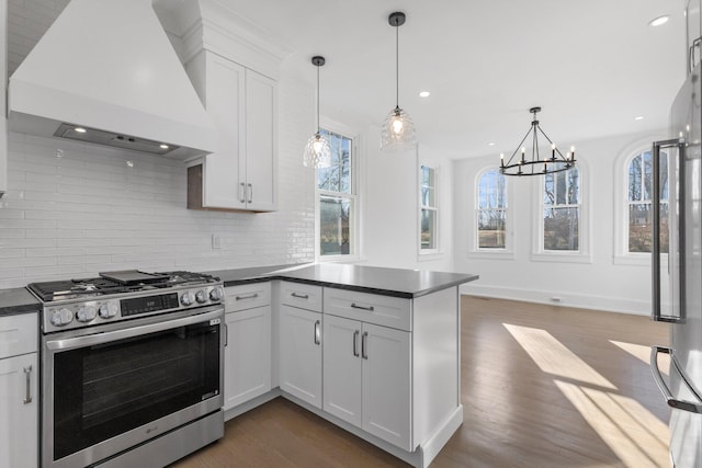 kitchen with tasteful backsplash, dark countertops, gas range, premium range hood, and a peninsula