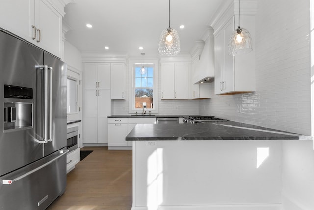 kitchen featuring a peninsula, high end refrigerator, a sink, decorative backsplash, and dark countertops