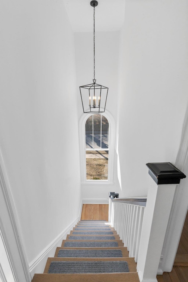 staircase with an inviting chandelier, a high ceiling, baseboards, and wood finished floors