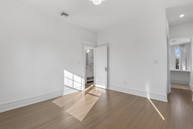 empty room with wood-type flooring, visible vents, and baseboards