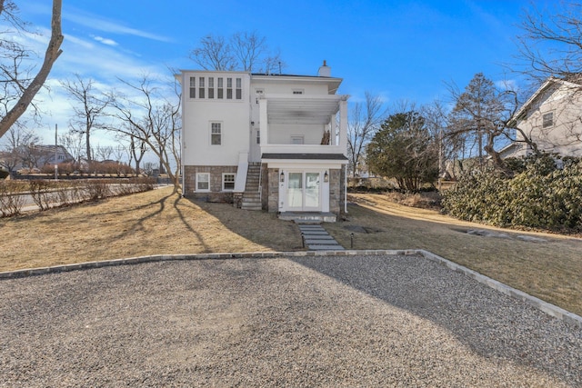 view of front facade with a balcony, stone siding, stucco siding, a front lawn, and a chimney