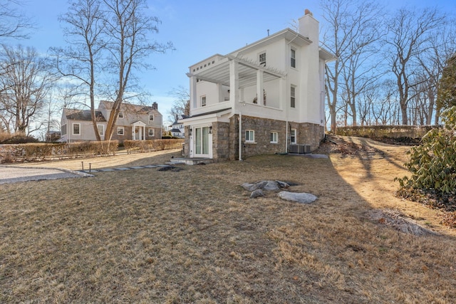 exterior space with a chimney, central air condition unit, stucco siding, a lawn, and stone siding