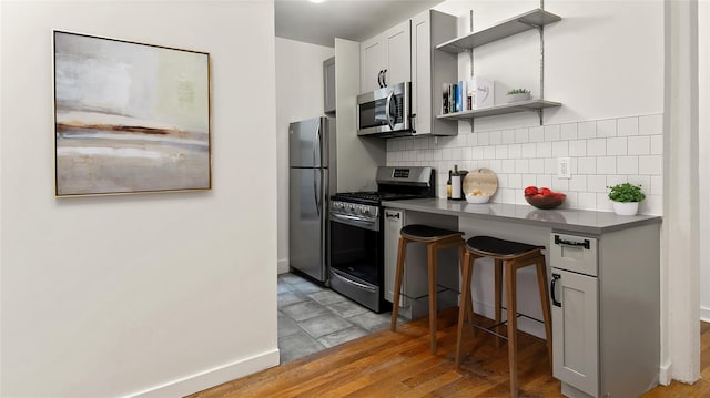 kitchen with baseboards, light wood-style flooring, appliances with stainless steel finishes, open shelves, and backsplash