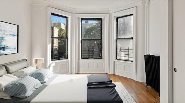 bedroom featuring radiator, a decorative wall, and wood finished floors