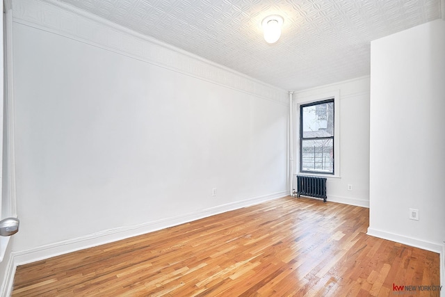 empty room featuring radiator heating unit, light wood-type flooring, and baseboards