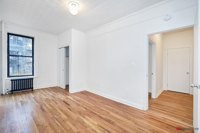 unfurnished bedroom with light wood finished floors, radiator heating unit, and baseboards