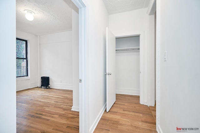 corridor featuring radiator, a textured ceiling, baseboards, and wood finished floors