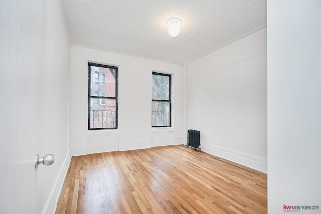 unfurnished room with baseboards, hardwood / wood-style floors, radiator heating unit, and a textured ceiling