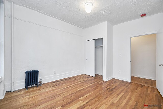 unfurnished bedroom with radiator, light wood-type flooring, a textured ceiling, and a closet