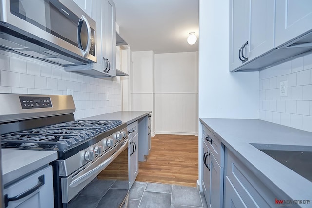 kitchen featuring a sink, light wood-style floors, light countertops, appliances with stainless steel finishes, and tasteful backsplash