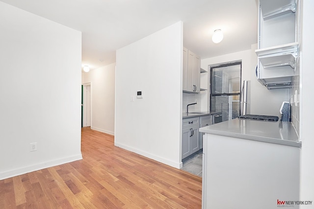 kitchen featuring a sink, baseboards, decorative backsplash, open shelves, and light wood finished floors